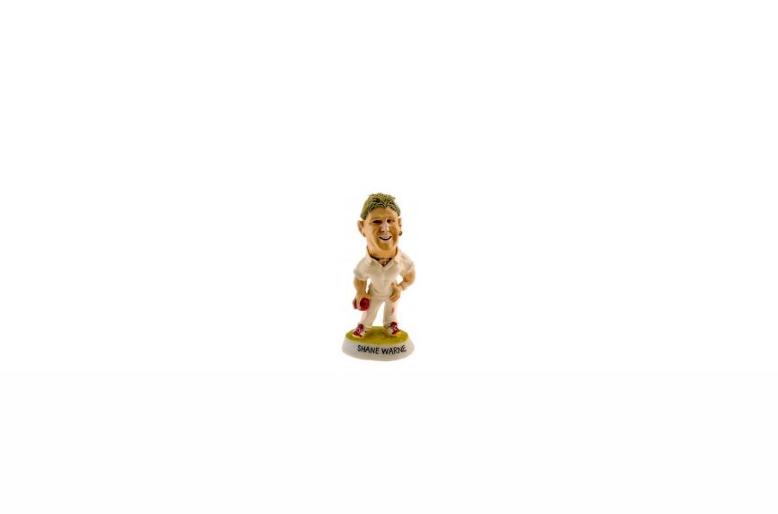 A small figurine of a cricketer in a white uniform holding a red ball stands on a base labeled "SHANE WARNE." Expertly crafted using Manufacturing Polyresin Products in China, it is showcased against a white background.