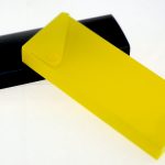 A black rectangular box and a yellow translucent plastic case with a snap button, commonly found when manufacturing stationery items in China, overlap on a white surface.