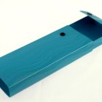 A blue rectangular box, often used for manufacturing stationery items in China, features a hinged lid partially open to reveal its interior. A black button accents the lid.