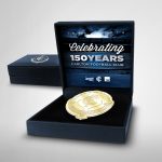 A gold commemorative medal in a display box marked โCelebrating 150 Years, Carlton Football Club,โ with another closed box in the background.