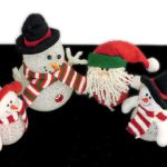 Four plush Christmas decorations, including two snowmen, Santa Claus, and a snowwoman, all wearing striped red and green scarves and hats, against a black and white background.