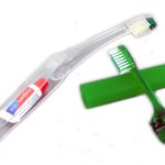 A travel toothbrush set with a small tube of toothpaste in a clear case, next to a green toothbrush with its own protective cover.