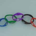 Five silicone wristbands in blue, green, purple, black, and red are arranged on a plain white background. Each band has an embedded hologram disc.