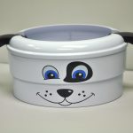 White round container with a dog face design, featuring blue eyes, black spots, and two black ears attached on the sides, placed on a plain background.