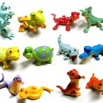 A collection of colorful plastic toy animals, including frogs, lizards, turtles, snakes, an otter, and a crocodile, displayed on a white background.