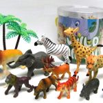 A collection of plastic toy wild animals, including a lion, giraffe, zebra, elephant, and others, arranged in front of a clear container with illustrated packaging and two plastic palm trees.
