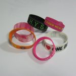 Six colorful silicone wristbands with various texts and symbols are arranged on a plain white surface.