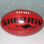 A red Sherrin Kangaroo Brand Australian rules football is displayed against a plain background.