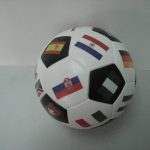 A soccer ball featuring flags of various countries on each white panel, placed on a plain gray surface with a light gray background.