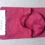 A maroon two-piece bath mat set with a rectangular mat and a matching contour mat, displayed on a grey carpeted surface.