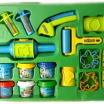 A green tray holds various plastic playdough tools, rolling pins, cutters, and multiple small tubs of colored modeling clay.