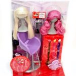 A doll hairstyling set with two mannequin heads, one with blonde hair, one with pink hair, chairs, hair accessories, and styling tools in purple and red packaging.