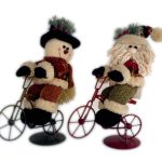 Two festive plush figures, a snowman and a Santa Claus, are riding small metal bicycles decorated for the holidays.