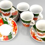 Six coffee cups and matching saucers with coffee bean and "Coffee" text design, arranged on a plain grey surface.