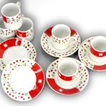 A set of four white cups and saucers with red and floral patterns, alongside four matching plates, arranged on a white background.