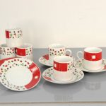 A set of cups and saucers with red and floral patterns arranged on a flat surface, including stacked cups and plates.