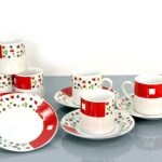 A set of four white ceramic cups with matching saucers, decorated with red squares and small floral patterns, arranged on a reflective surface.