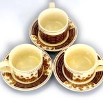 Three empty cappuccino cups with matching saucers, decorated with coffee beans and text, arranged in a triangular formation on a white surface.