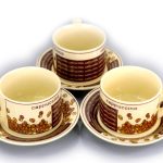 Three ceramic cappuccino cups with matching saucers, decorated with coffee bean and text patterns, arranged in a triangular formation.