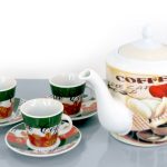 A ceramic teapot labeled "coffee" with two matching cups and saucers, all decorated with coffee beans and leaves, on a gray surface.