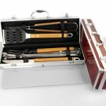 A metal and wood barbecue tool set, including tongs, spatula, and fork, displayed in an open silver storage case on a white surface.