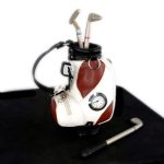 A miniature golf bag with a watch embedded on its side, holding three miniature golf clubs, and a pen shaped like a golf club lying beside it.