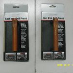 Two identical packaged cast iron grill presses with brown handles are displayed side by side on a white surface. The packaging includes product name, description, and images.