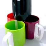 Four colorful ceramic mugsโblack, red, green, and maroonโare stacked together, with the black mug placed on top of the others.