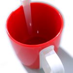 A red plastic cup with a white handle and a white plastic spoon inside, photographed from above on a white background.