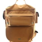 Tan canvas backpack with multiple external pockets, black side straps, and a top handle, displayed against a white background.