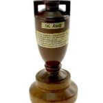 A small brown urn-shaped Ashes cricket trophy with a label and wooden base, photographed against a white background.