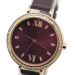 A brown wristwatch with a round face, Roman numerals at 12 and 6, and a jeweled bezel, featuring a brown leather strap.