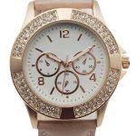 Gold wristwatch with a light brown leather strap, crystal-studded bezel, and white face displaying three subdials and gold hour markers.