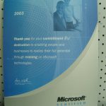 A 2003 Microsoft Certified Technical Education Center plaque featuring a business-themed image and a message about commitment, dedication, and training in Microsoft technologies.