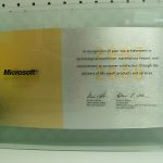 A Microsoft Gold Certified Partner plaque recognizing achievement in technological excellence and customer satisfaction, mounted on a transparent display.