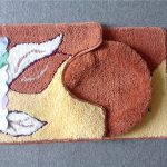 A set of two colorful bathroom rugs with leaf patterns, one U-shaped and one round, placed on a gray floor. The packaging label reads "Suya.