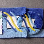 Three blue and white patterned bathroom mats, including a rectangular mat, a contour mat, and a toilet lid cover, are displayed on a gray surface with a Suya brand label.
