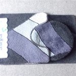 A set of three rectangular and circular bath mats with geometric patterns in shades of black, gray, and white displayed on a gray surface.