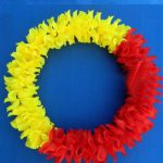 A lei made of yellow and red artificial flowers is arranged in a circular shape against a blue background.