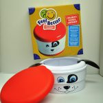 A children's sickness container shaped like a dog with a red lid, in front of its packaging labeled "Feel Better Friends.